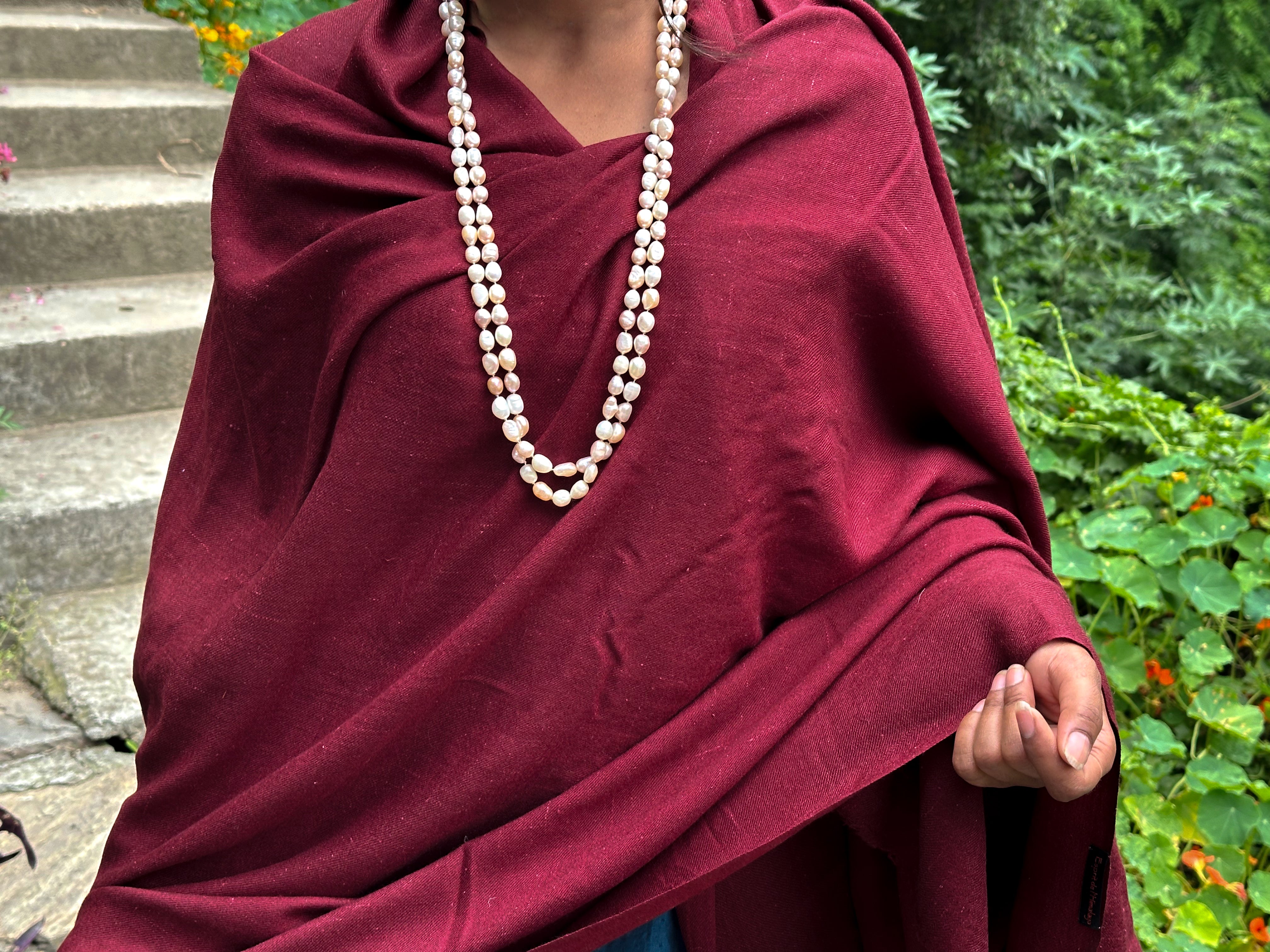 Detail shot of an burgundy shawl with a woman's hand and pearl bracelet resting on it.