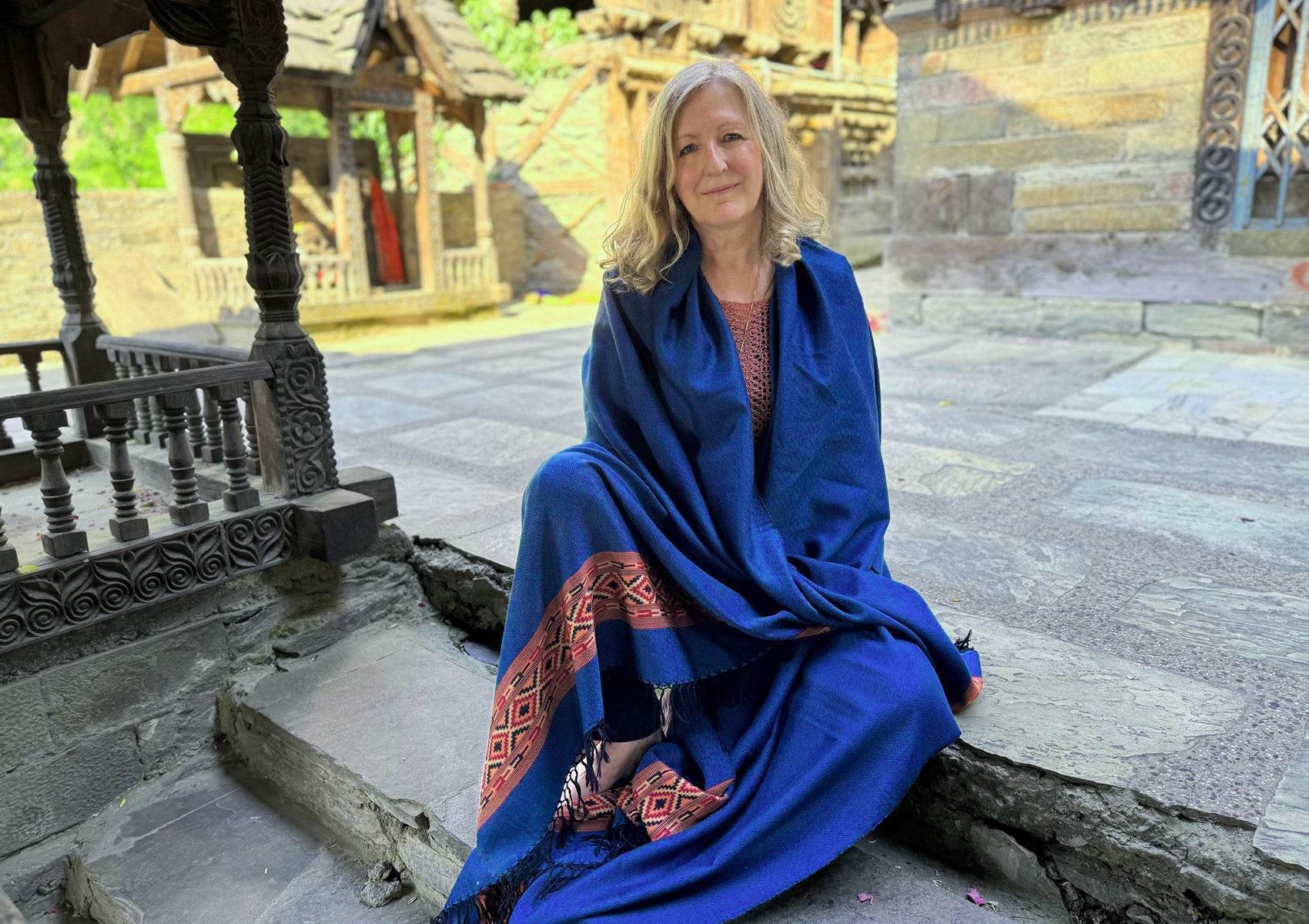 Femme assise dans la cour d’un temple portant le châle DEVA bleu royal en laine mérinos avec design ethnique.