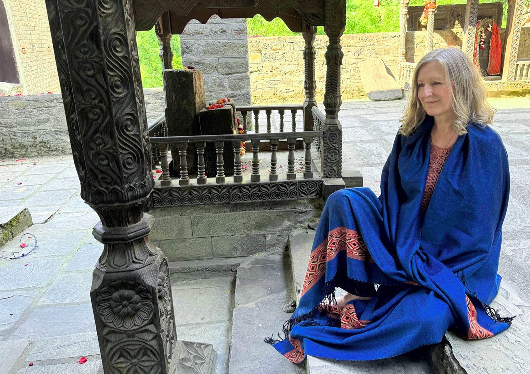 Femme assise dans la cour d’un temple portant le châle DEVA bleu royal en laine mérinos avec design ethnique