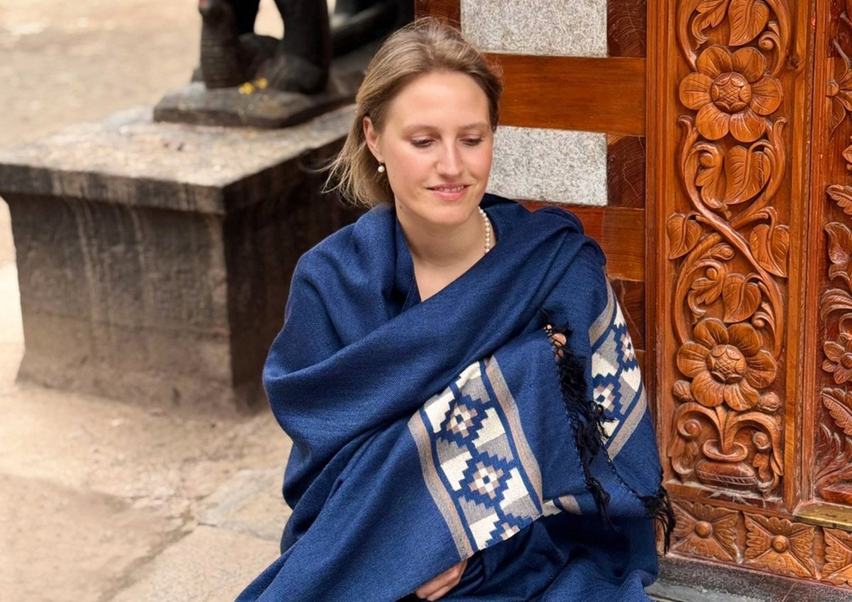 Woman seated in meditation wearing the Esprit de l’Himalaya Mahadev Shawl, large blue handwoven wool with ethnic border.
