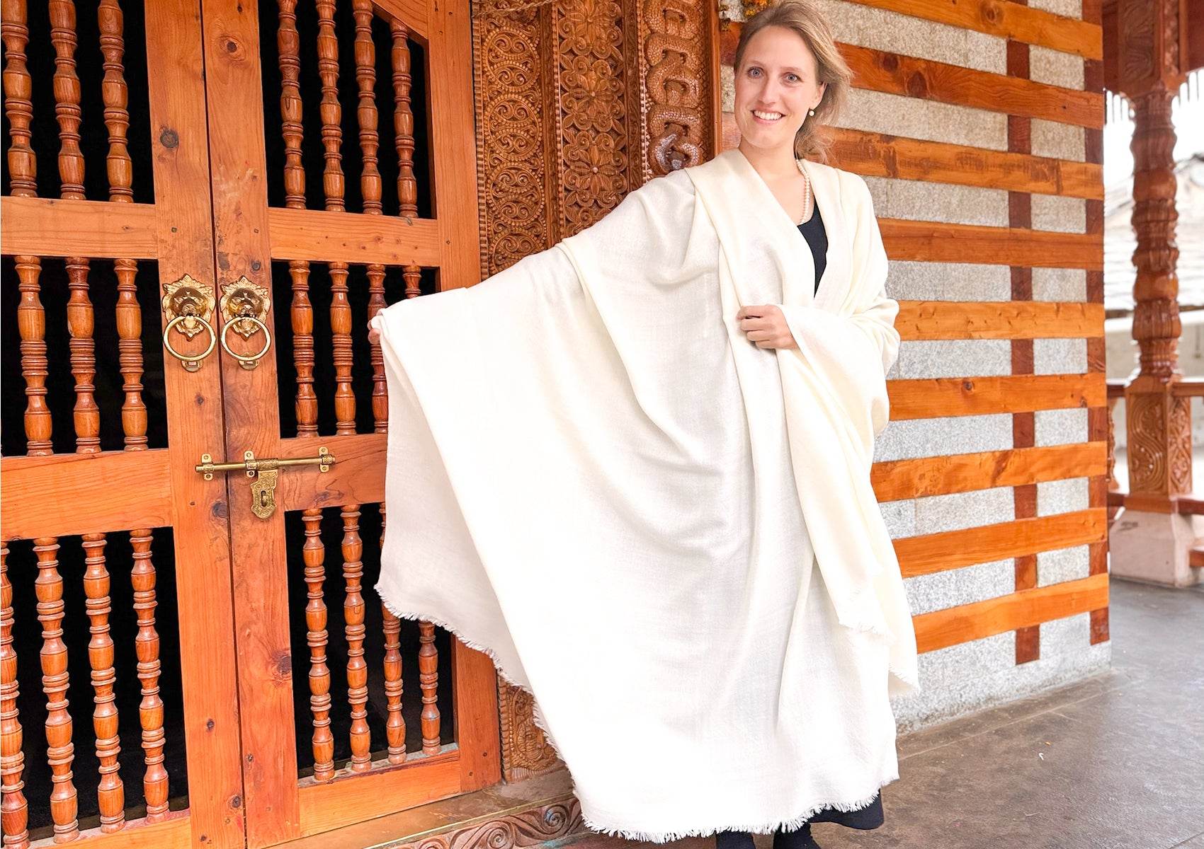 Full view of large cream wool meditation wrap, handwoven lama shawl displayed against ornate wooden temple architecture.