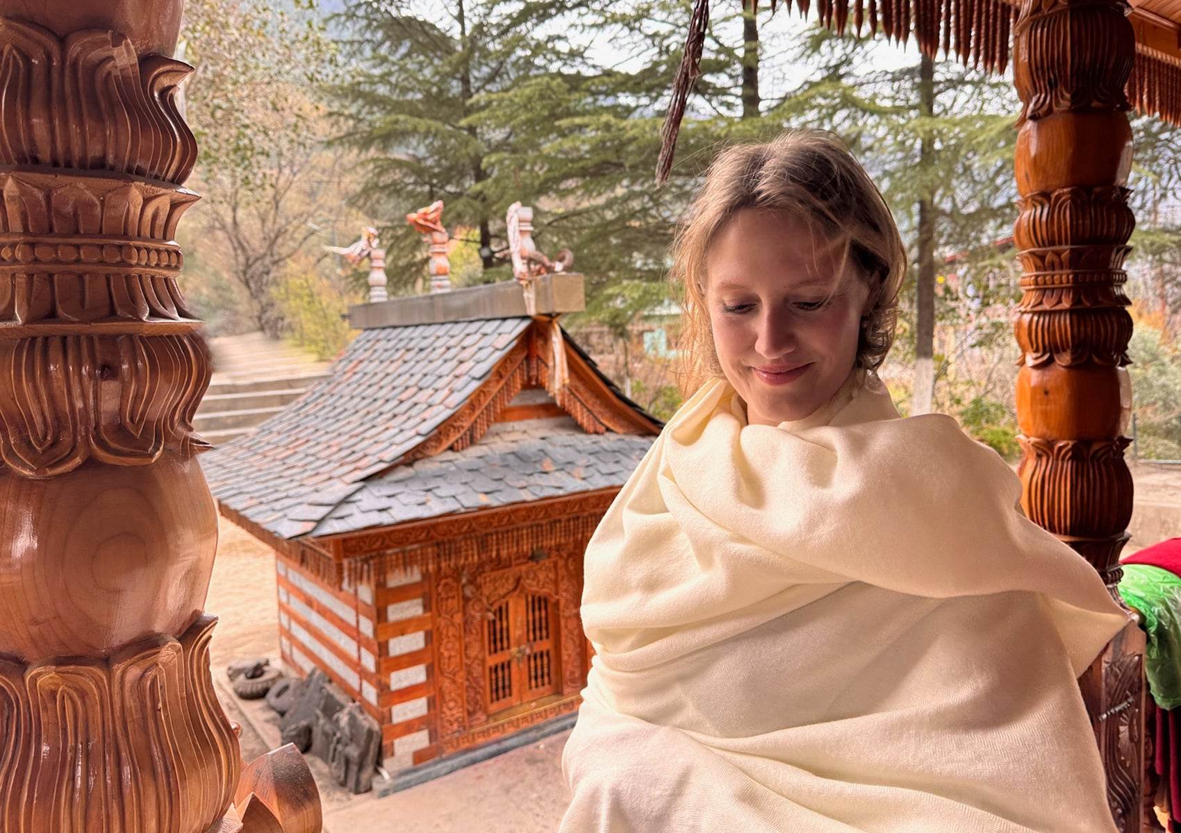 Woman standing in front of a carved wooden Himalayan temple door, draped in a cream lama meditation shawl made of soft merino wool.