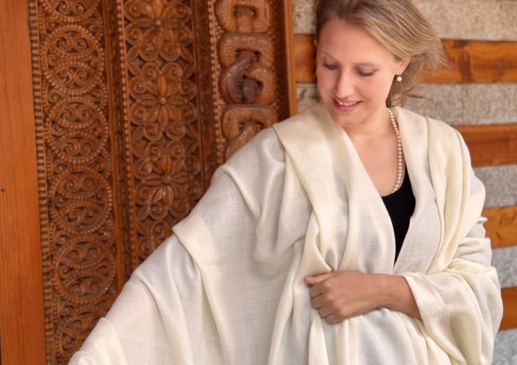 Spiritual scene of woman in cream lama shawl beside intricately carved wooden temple doorway.