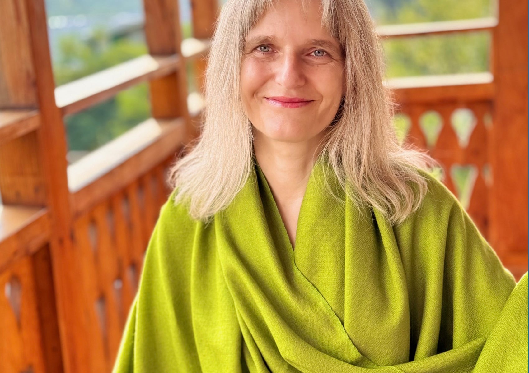 Woman smiling while wrapped in the Lama Green meditation shawl made from soft merino wool.