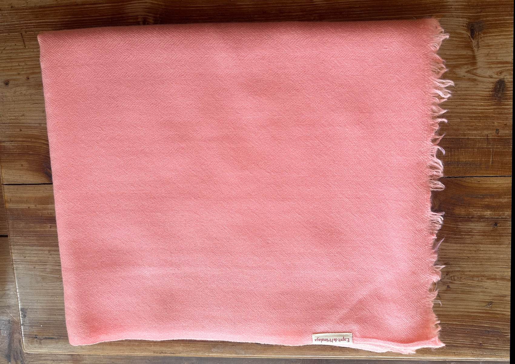 Folded peach LAMA meditation shawl in handwoven merino wool, displayed on wooden surface.
