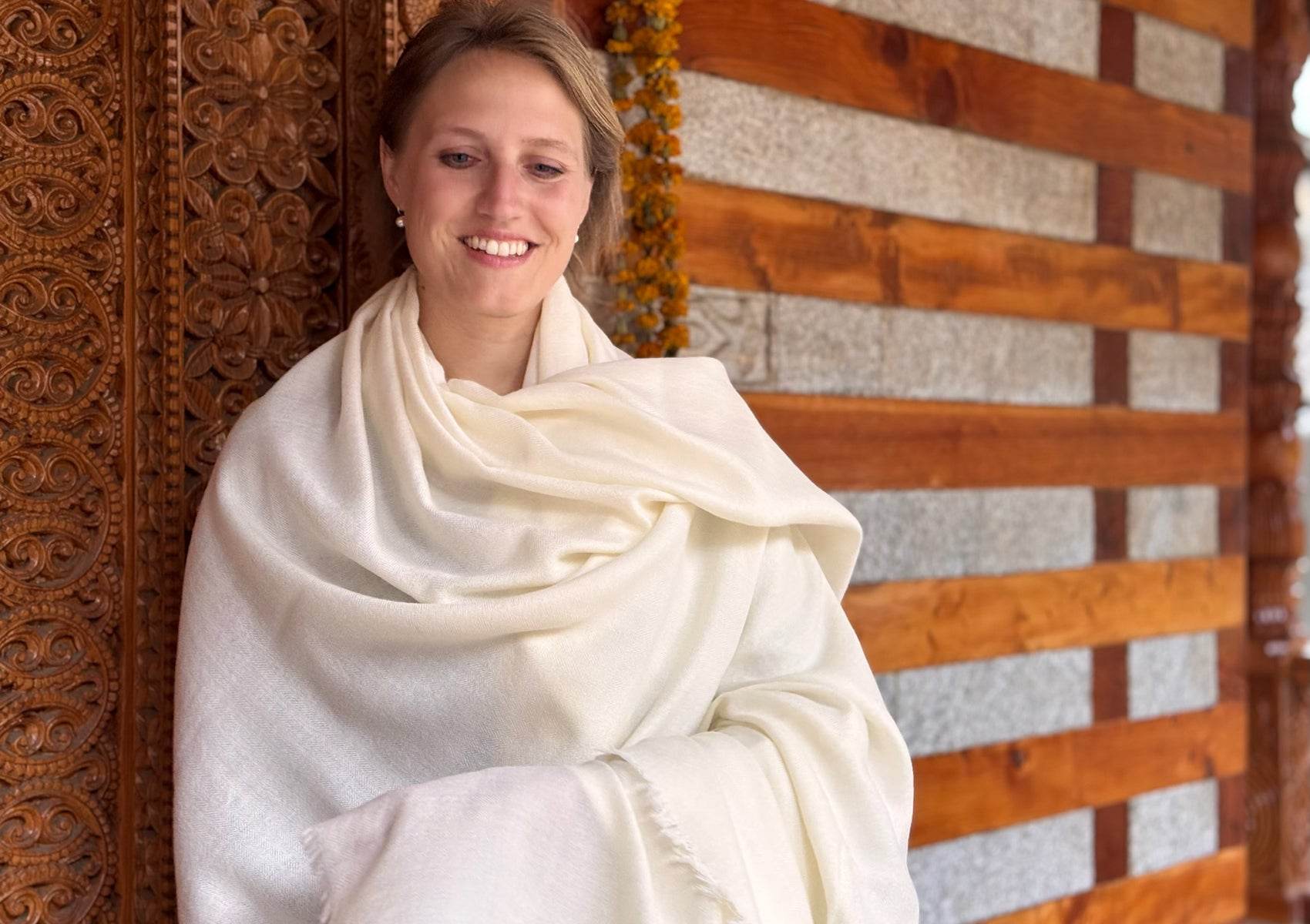 Soft cream lama shawl for meditation wrapped around shoulders of woman standing at a Himalayan temple.