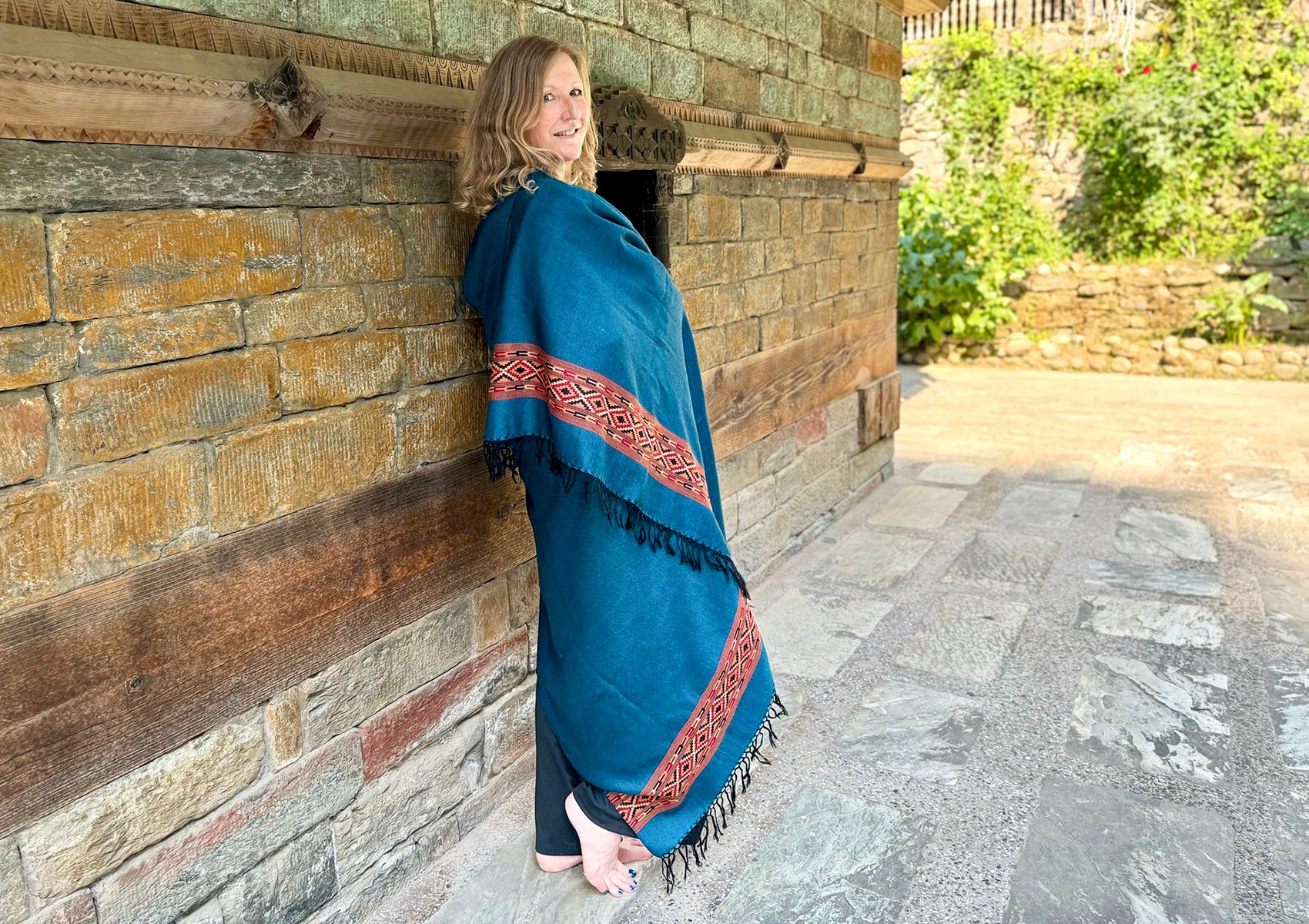 Woman wearing DEVA denim blue merino wool meditation shawl with Himalayan ethnic border leaning on a temple.