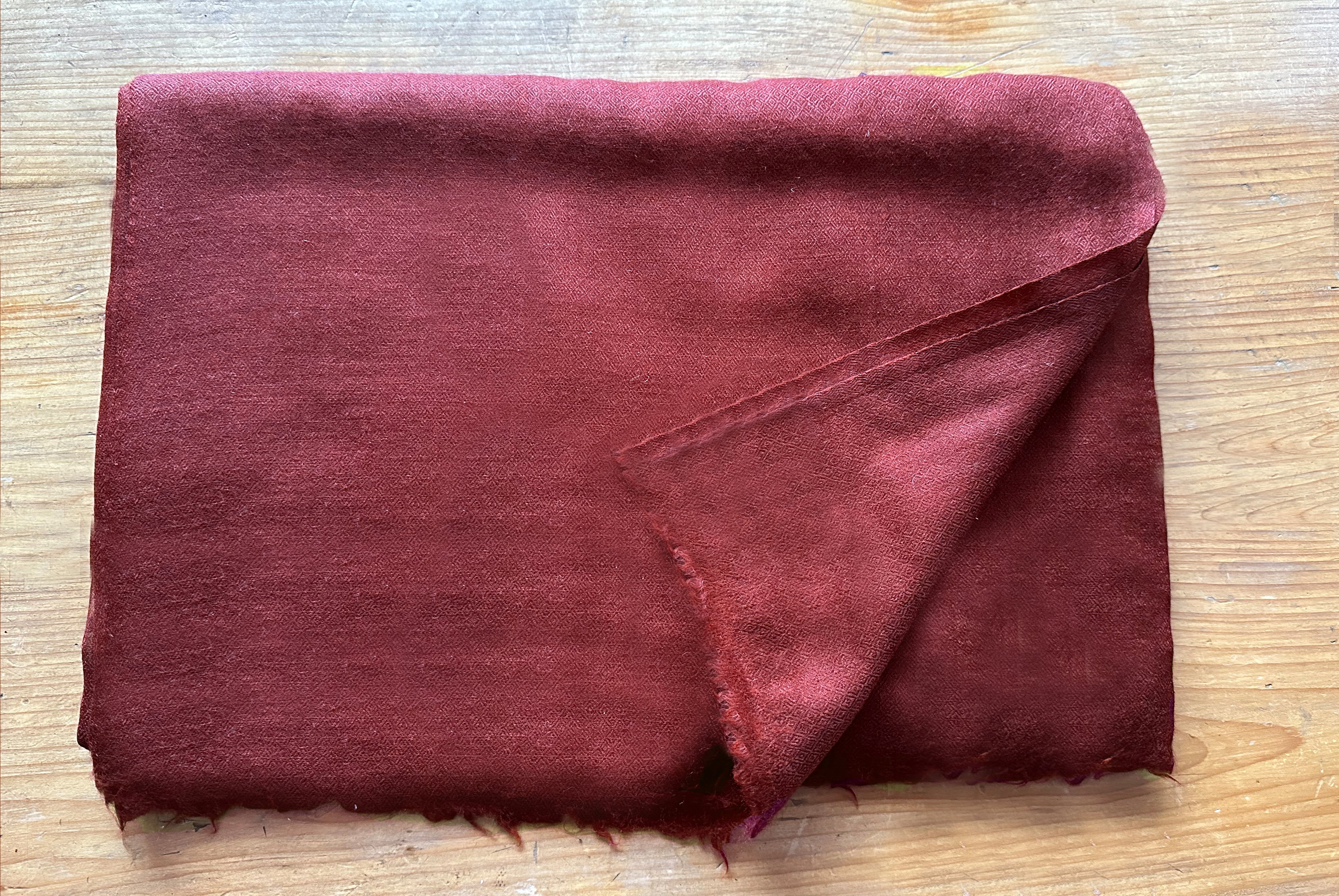 Close-up of a folded burgundy meditation shawl with a corner flipped to reveal the fine fabric texture, placed on a wooden surface.