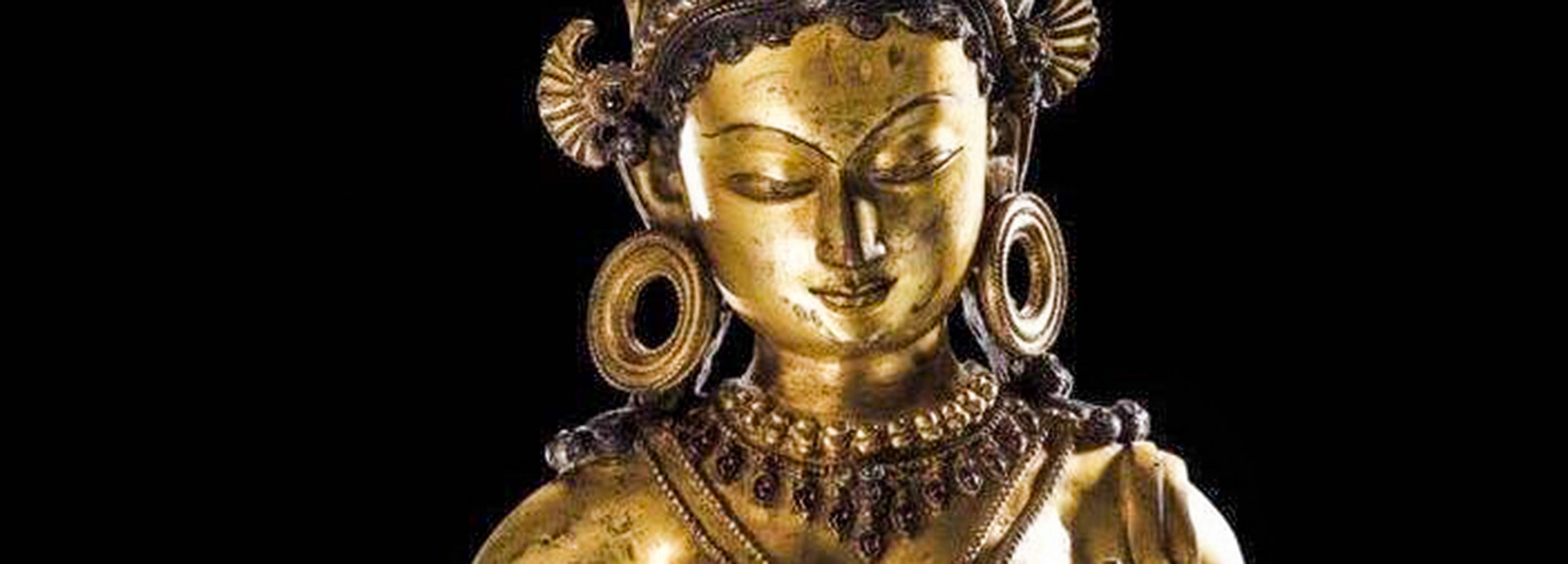 Close-up of a Nepalese Buddhist Tara statue from the 13th century, with intricate gold details and traditional jewelry on a black background.