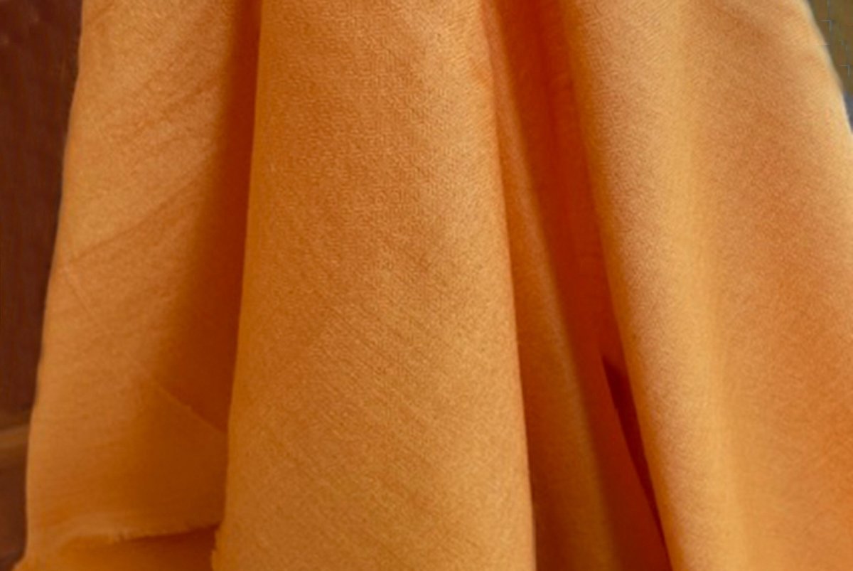 Detailed shot of an orange shawl fabric, highlighting its texture and warm color.
