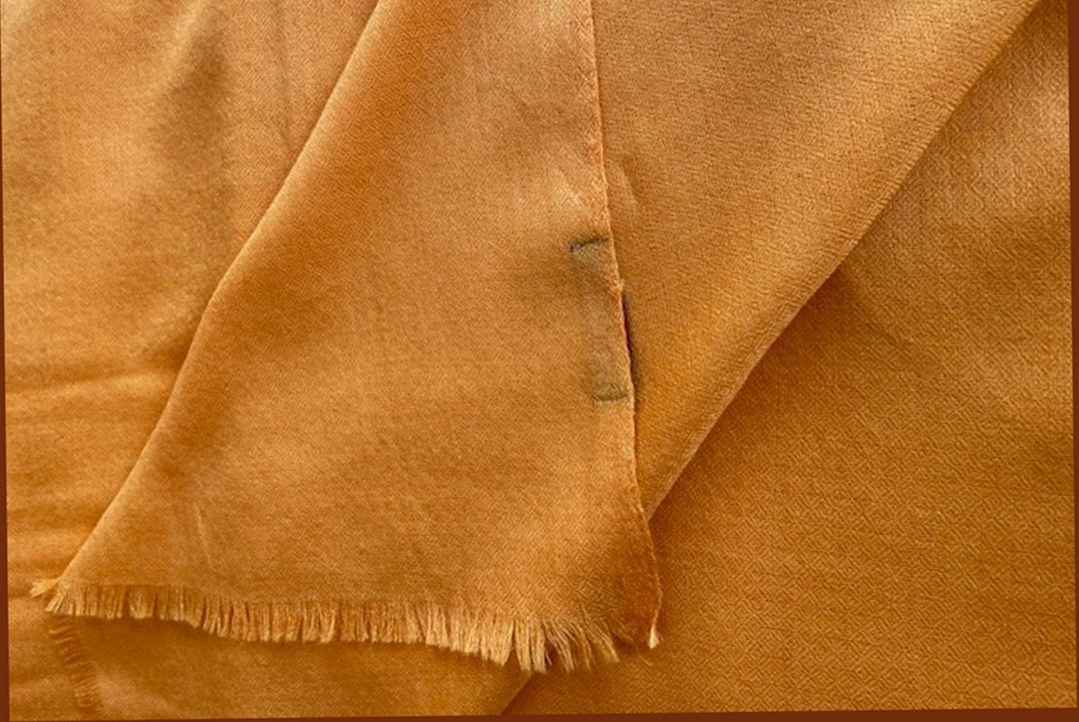Orange shawl fabric laid flat, emphasizing its soft and light material for comfort.