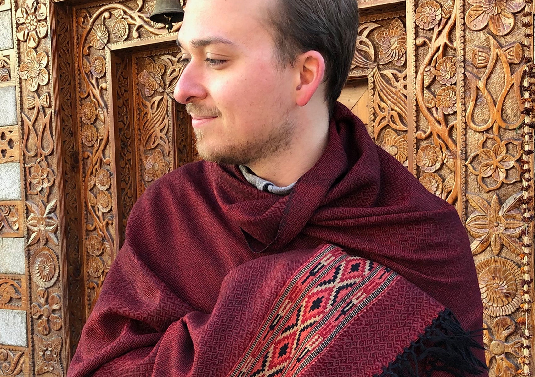 Man standing in front of carved temple wall wearing large DEVA dark red merino wool meditation shawl
