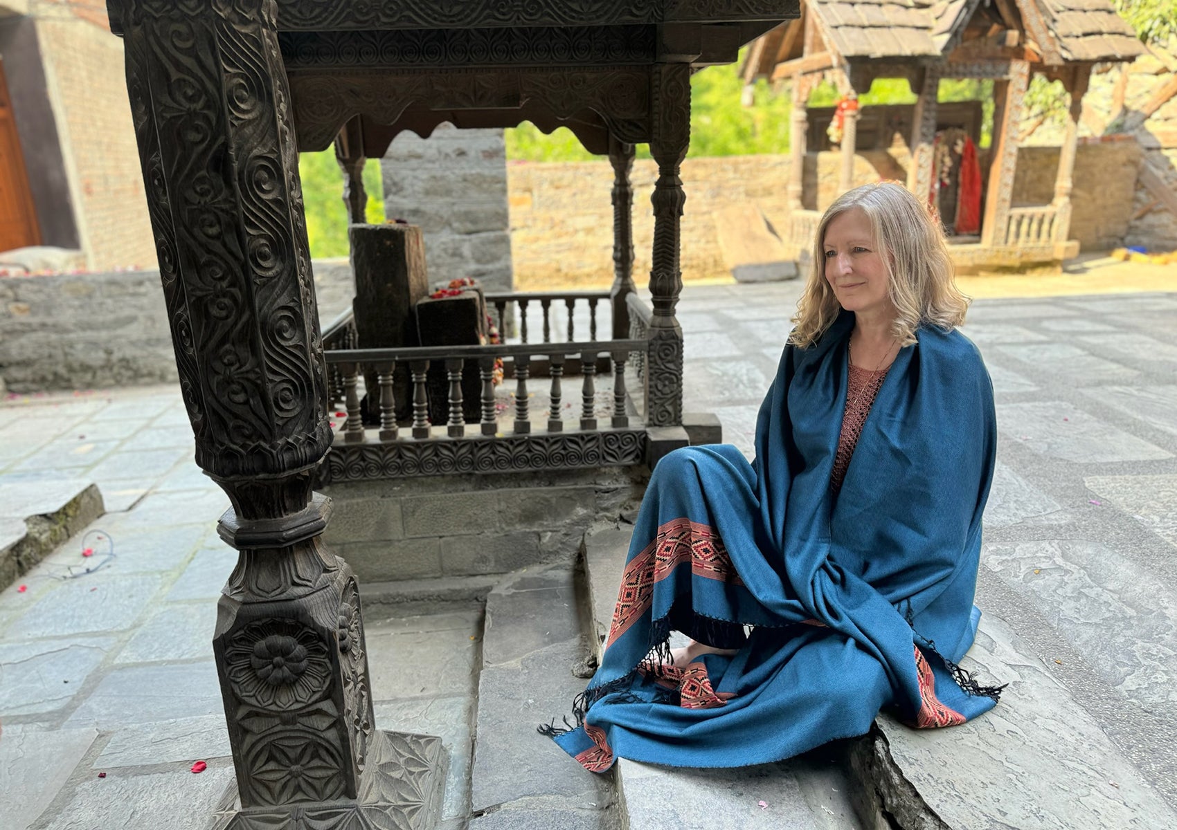 Woman wearing DEVA denim blue merino wool meditation shawl with Himalayan ethnic border near stone fireplace.