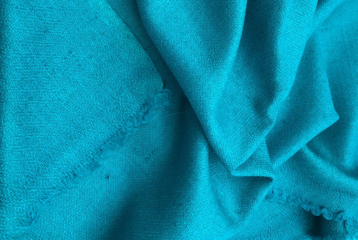 Detailed view of a turquoise silk pashmina shawl folded at the corner, showcasing its fine texture and cozy feel.
