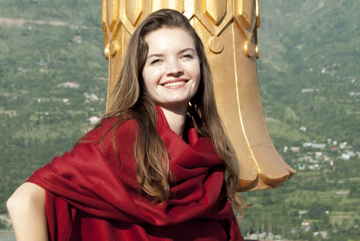 Person meditating on a temple rooftop, wrapped in a deep red shawl with a golden stupa.
