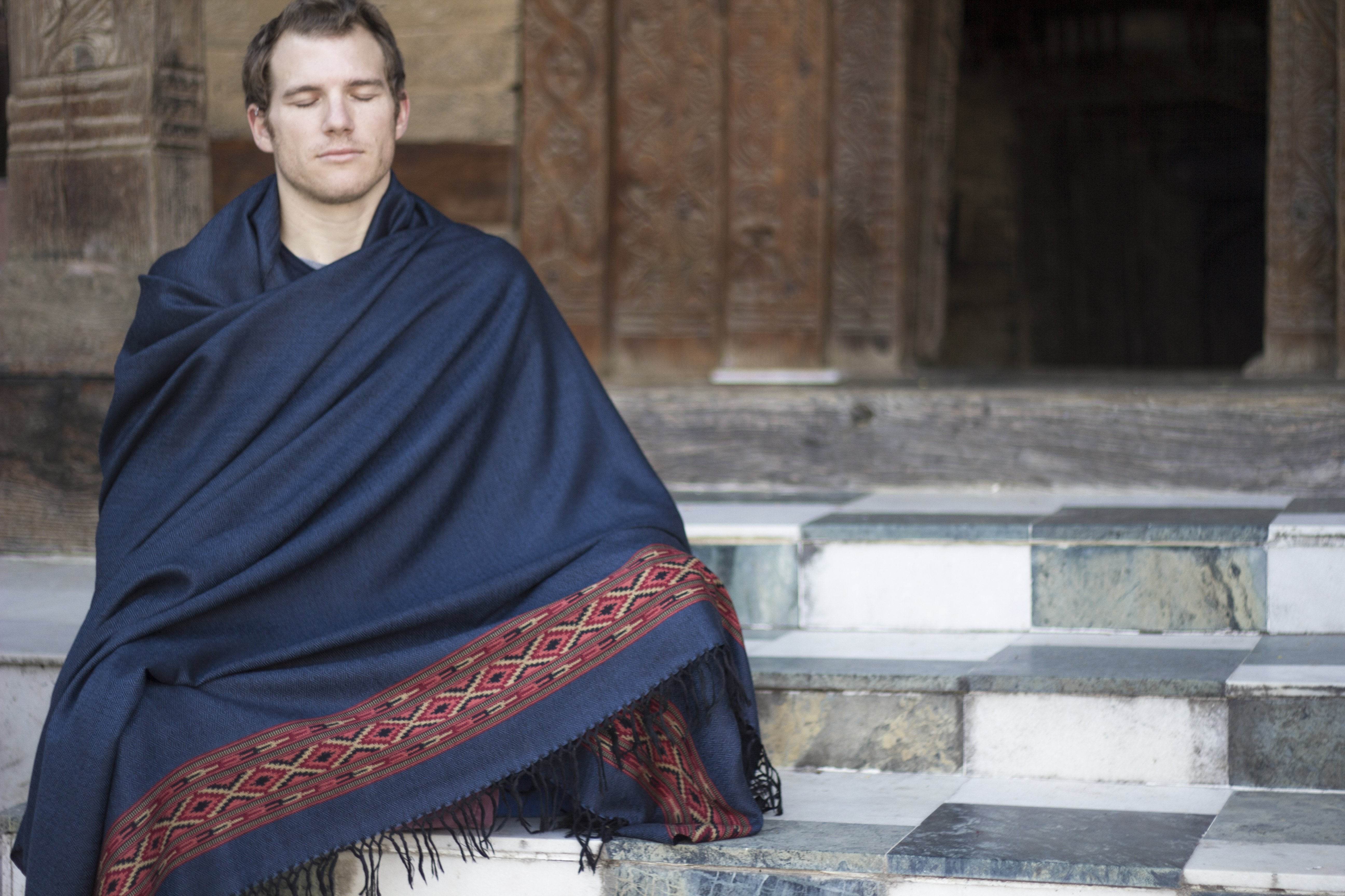 Man meditating on temple steps wrapped in DEVA Dark Blue meditation shawl with traditional ethnic border