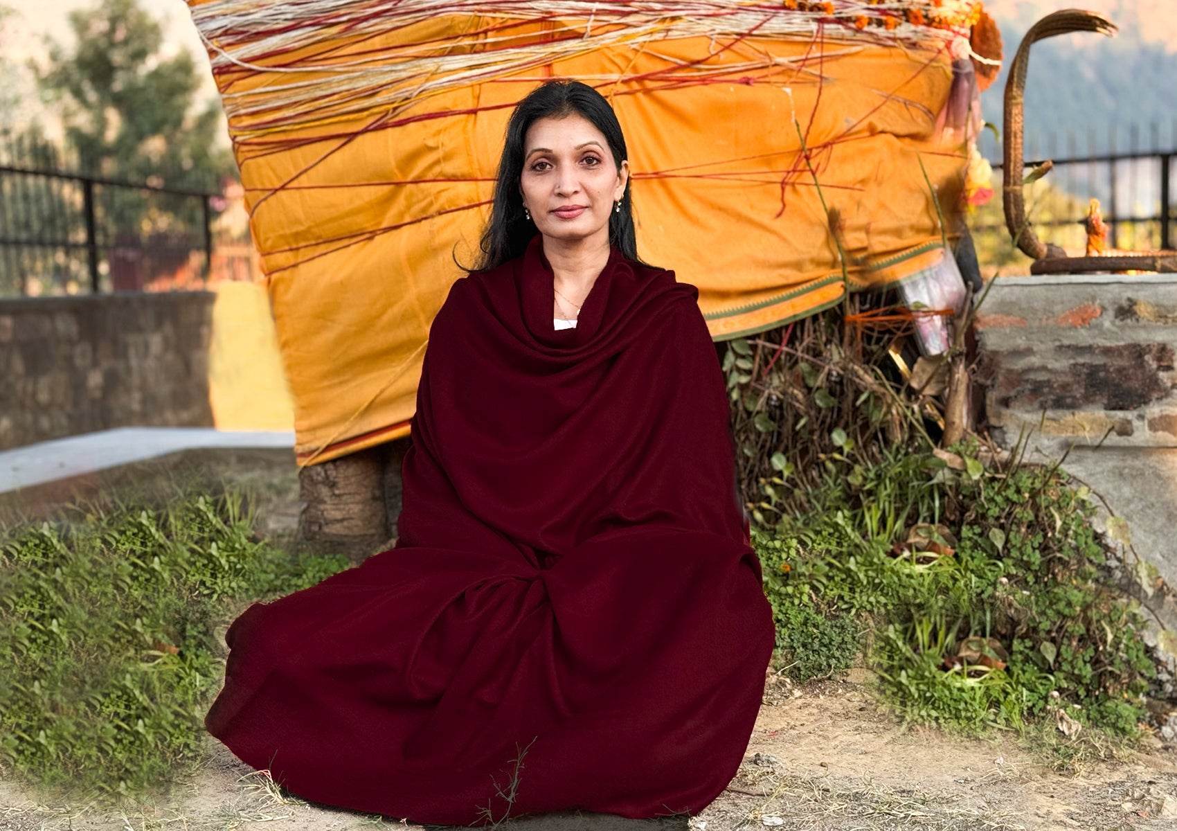 Lady wrapped in the Bodhi deep red burgundy large pashmina shawl sitting in front of a sacred temple tree.