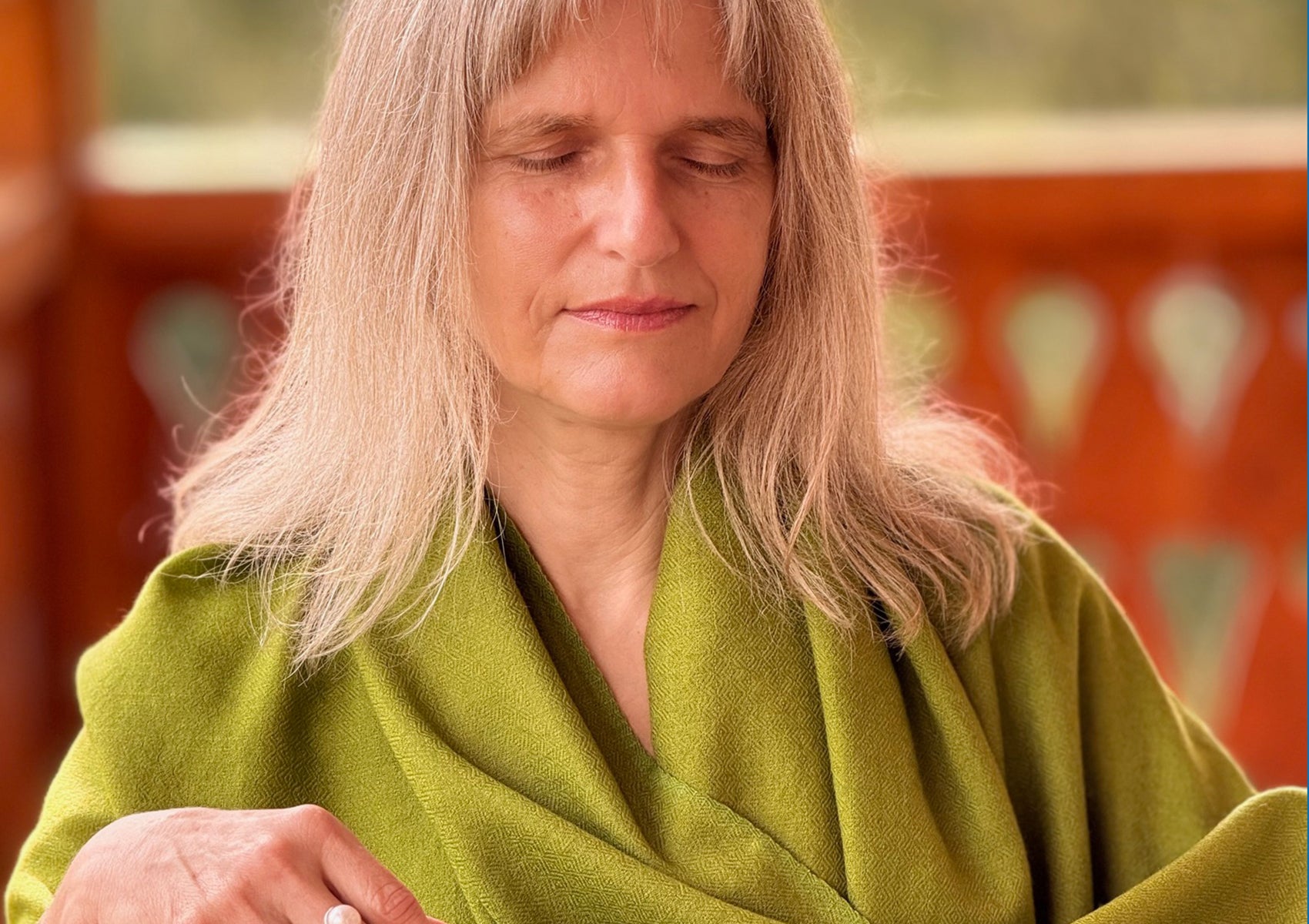 Woman meditating on a wooden balcony wearing the Lama Green meditation shawl in fine merino wool.