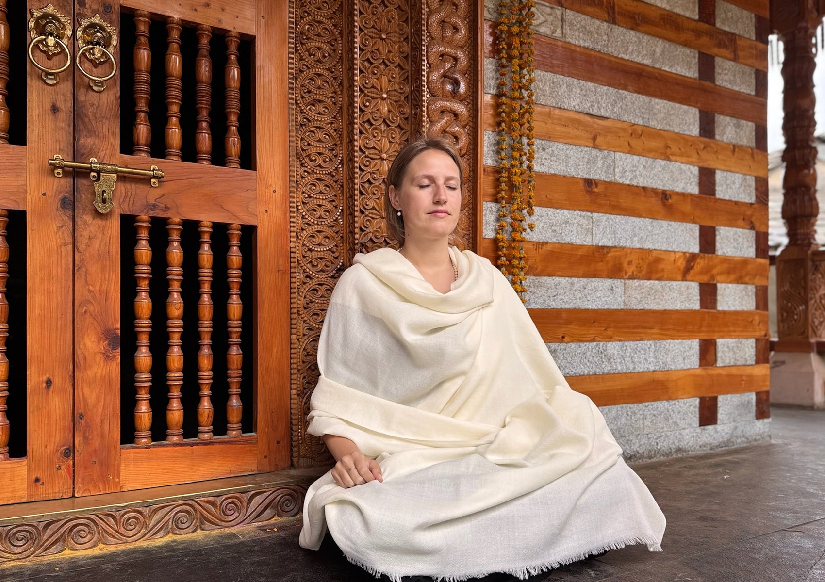 Woman meditating in a seated posture, wrapped in the LAMA cream shawl
