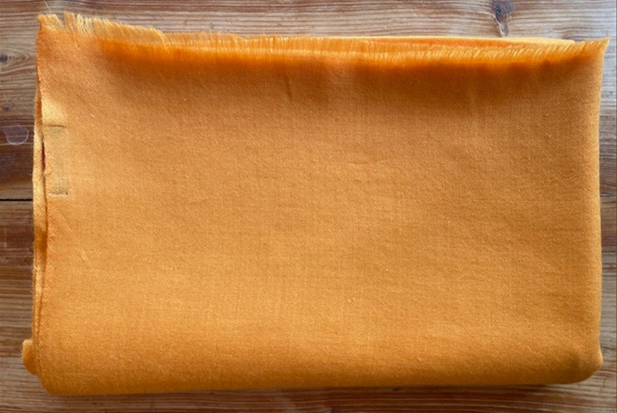 Folded orange fabric placed on a wooden surface, showcasing its texture and bright color.