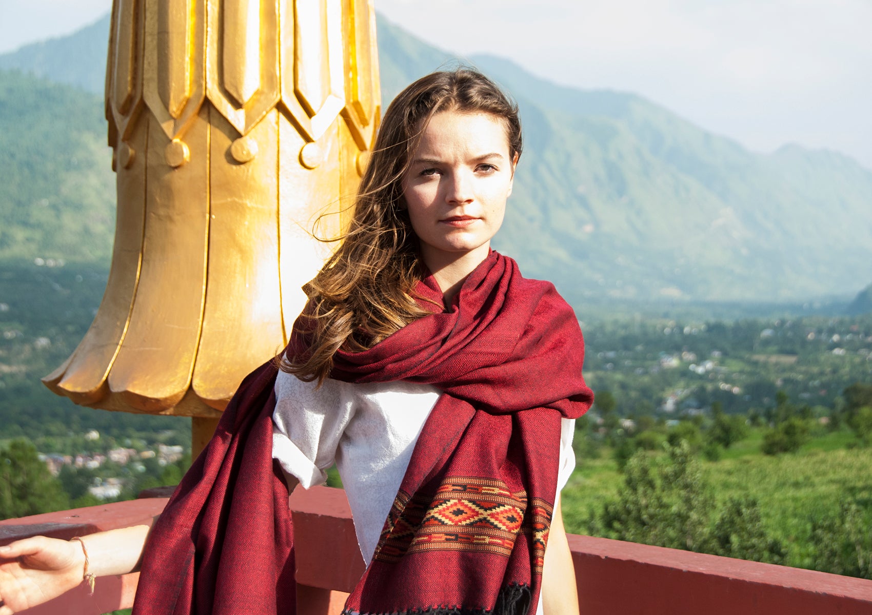 Woman draped in DEVA dark red merino wool meditation shawl with Himalayan border, standing before mountain view.
