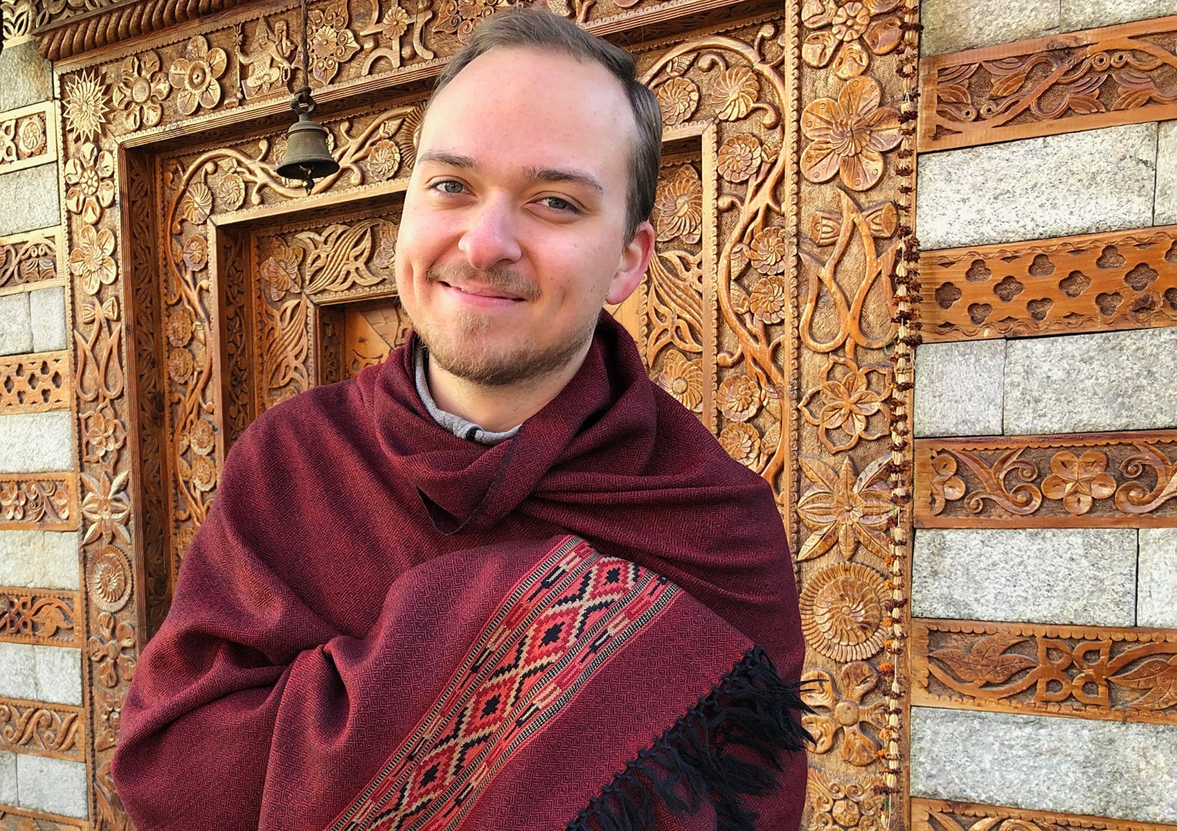Close-up of man wearing DEVA dark red merino wool meditation shawl with Kinnauri ethnic pattern.