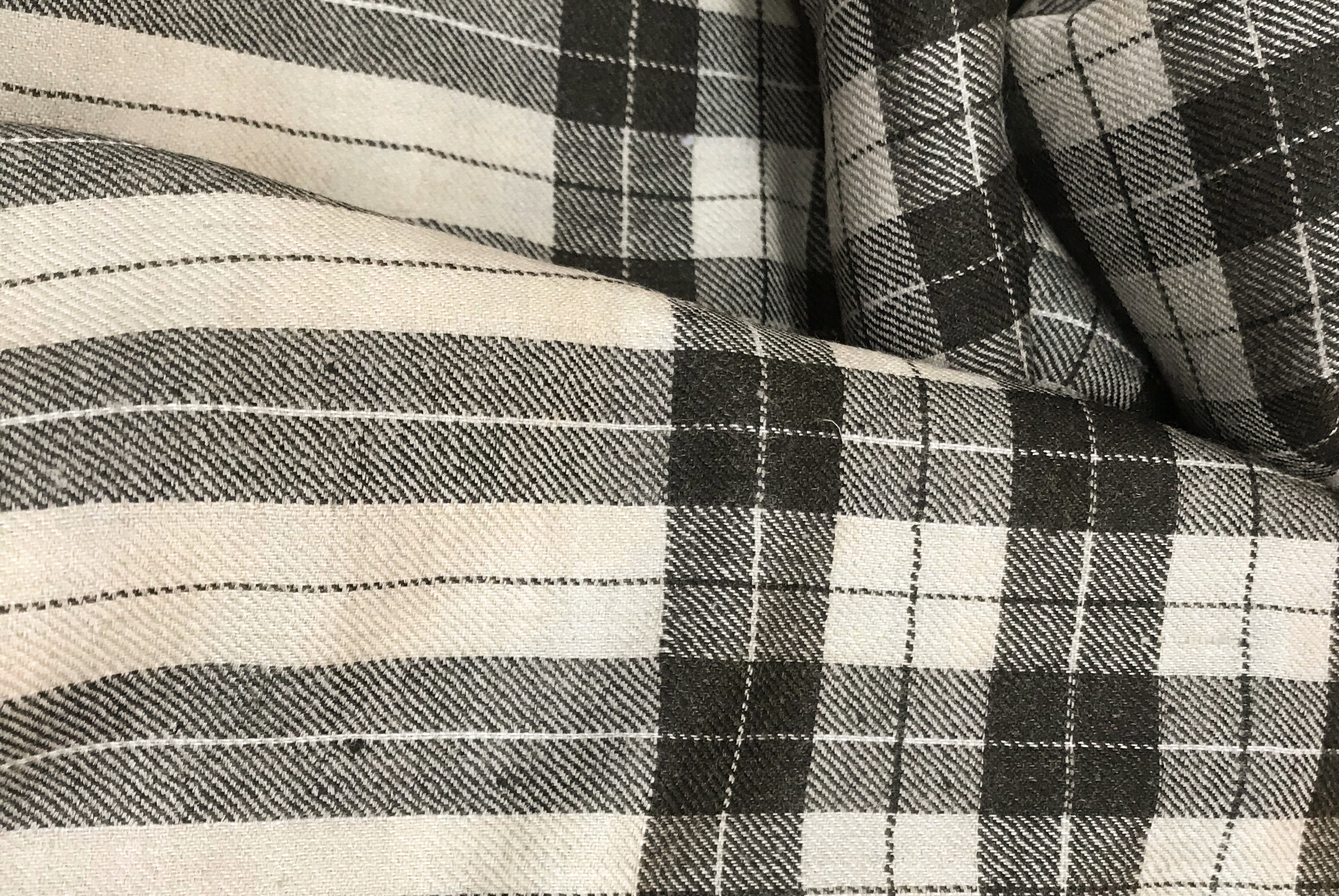 Detail of a black and beige checkered shawl, draped in soft folds, emphasizing its stylish design and comfortable fabric.