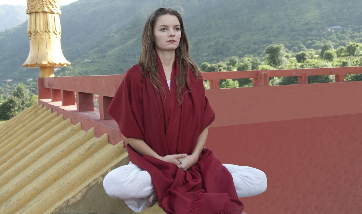 Meditative pose in a deep red shawl against a backdrop of Himalayan temple and nature.